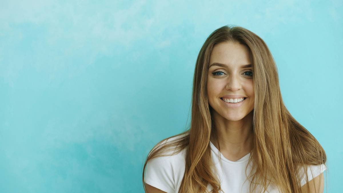 Closeup portrait of young smiling and cheerful woman looking into camera on blue background
