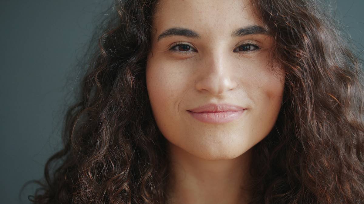 happy young mixed race lady smiling at camera alone on black background expressing good mood and happiness. Modern millennials and emotions concept.